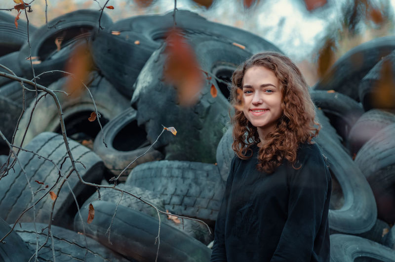 Cheerful curly-haired girl standing against a landfill of used car tires