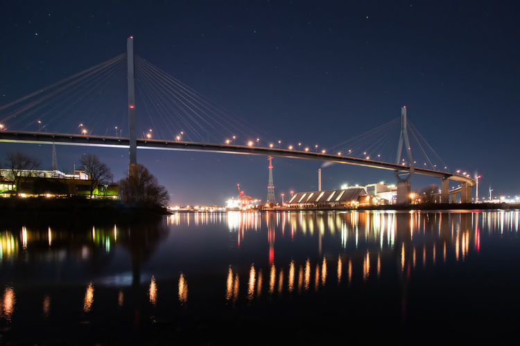 Illuminated bridge over river against sky at night