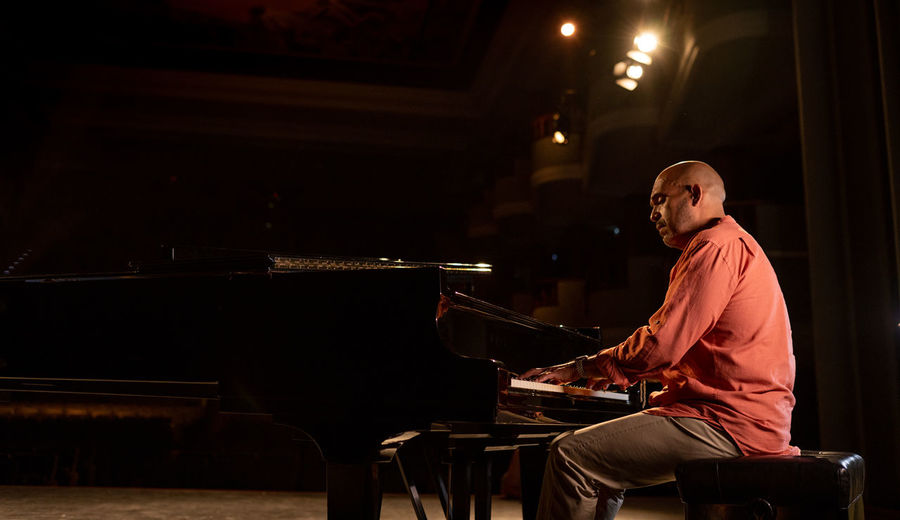 Side view of focus bald male musician playing piano during performance on obscure stage in theater