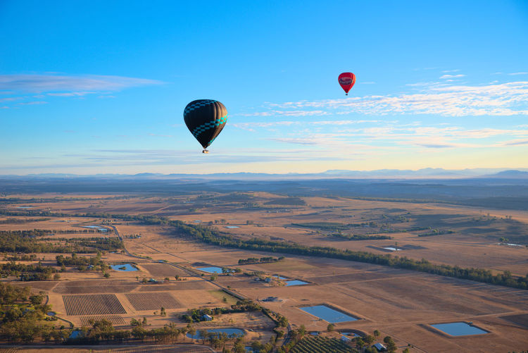 Hot air balloons flying over farm against blue sky