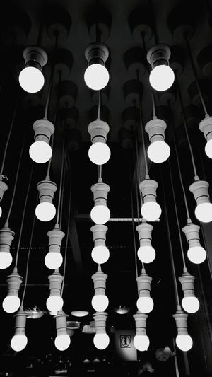 Low angle view of illuminated light bulb hanging against black background