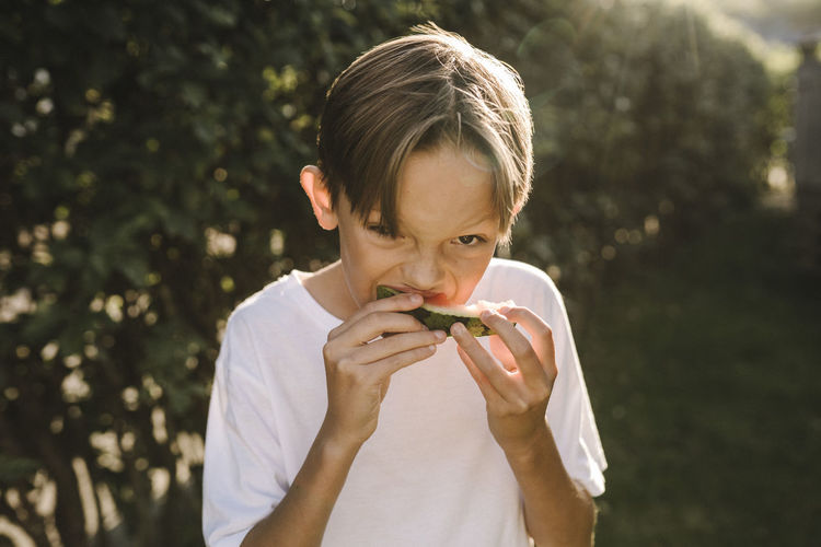 Boy eating watermelon while standing in back yard