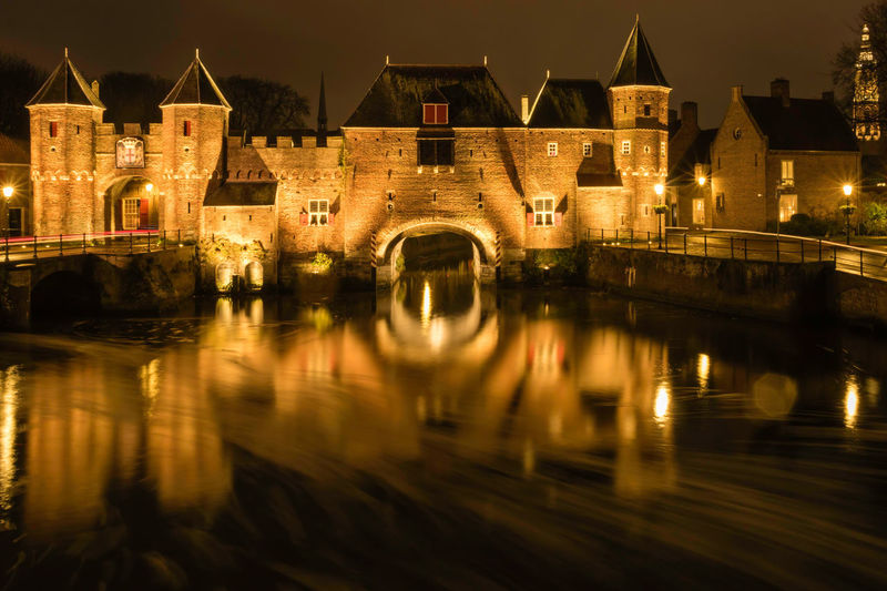 Illuminated medieval gateway koppelpoort at night reflecting in water, amersfoort the netherlands