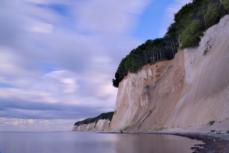 Scenic view of cliff at sea shore against sky