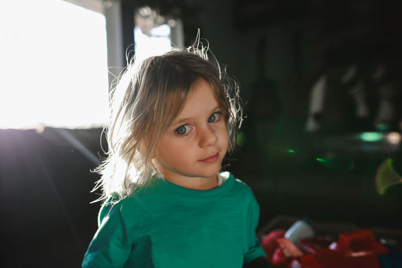 Little boy with long hair looking at camera with sunflare from window