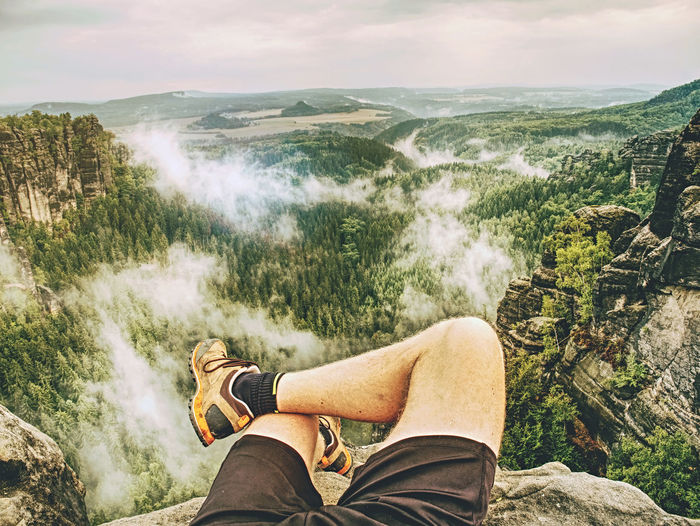 Hiker legs resting in rock  with fall nature in background. guy relax on mountain top and enjoy view