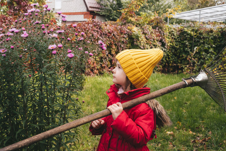 Child in the autumn garden with a rake, girl looks away at the flowers. seasonal garden work. 