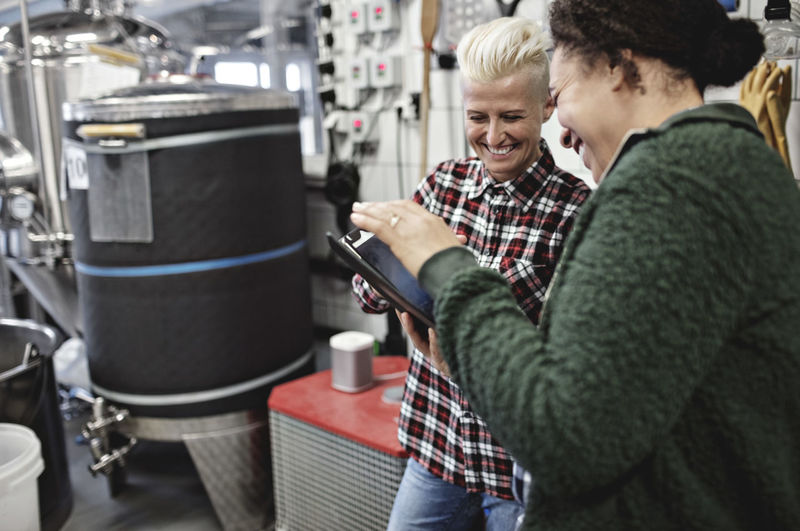 Smiling female workers discussing over digital tablet while working in brewery