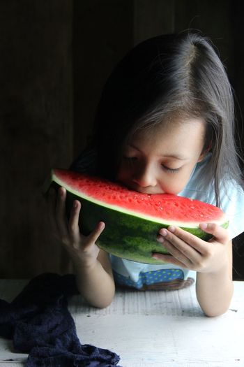 Close-up of little girl eating juicy watermelon against dark background