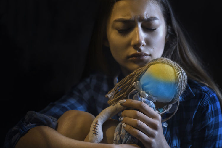 Woman holding doll against black background