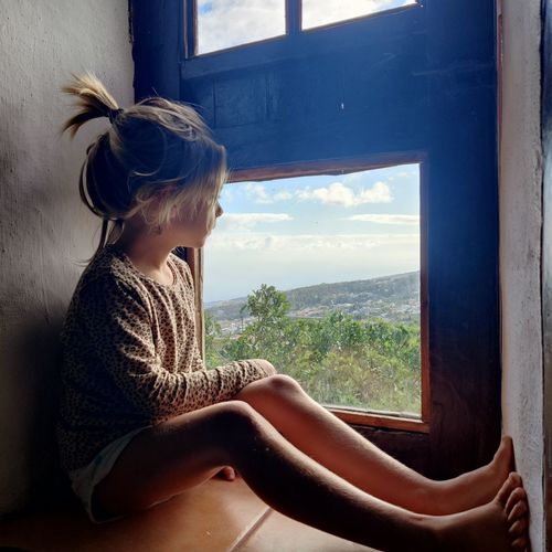 Side view of a little girl sitting and watching through the window