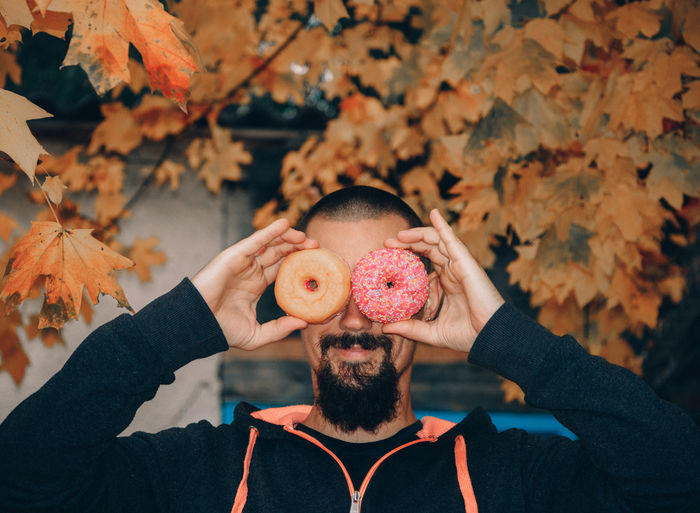 Man holding donuts against autumn leaves
