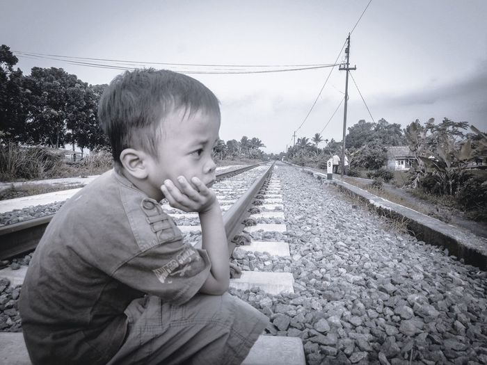 Boy on railroad track against sky