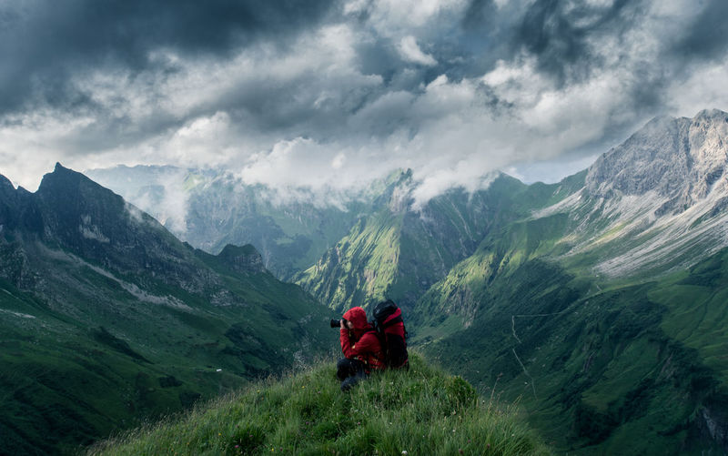 Woman sitting on mountain against cloudy sky