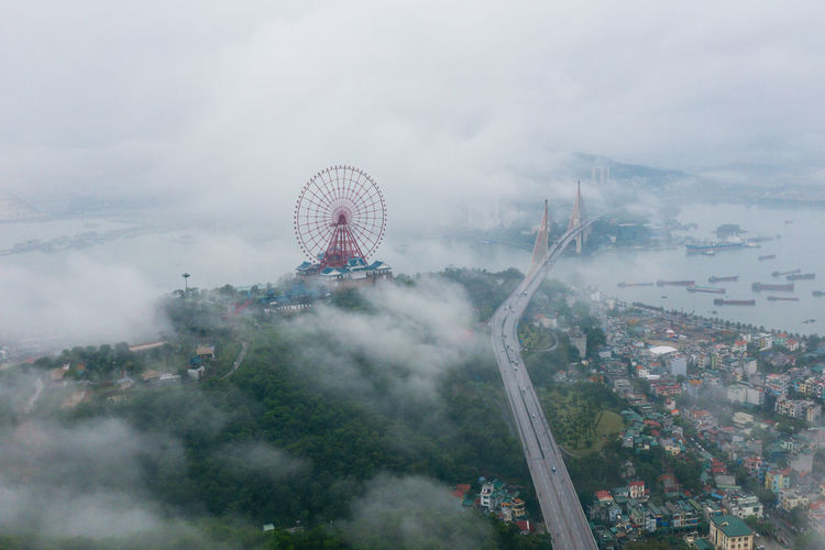Aerial view of ferris wheel and bridge in city during foggy weather