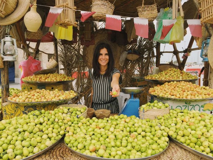 Portrait of smiling woman holding fruits for sale at market stall