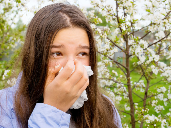 Close-up of girl covering mouth with tissue against tree