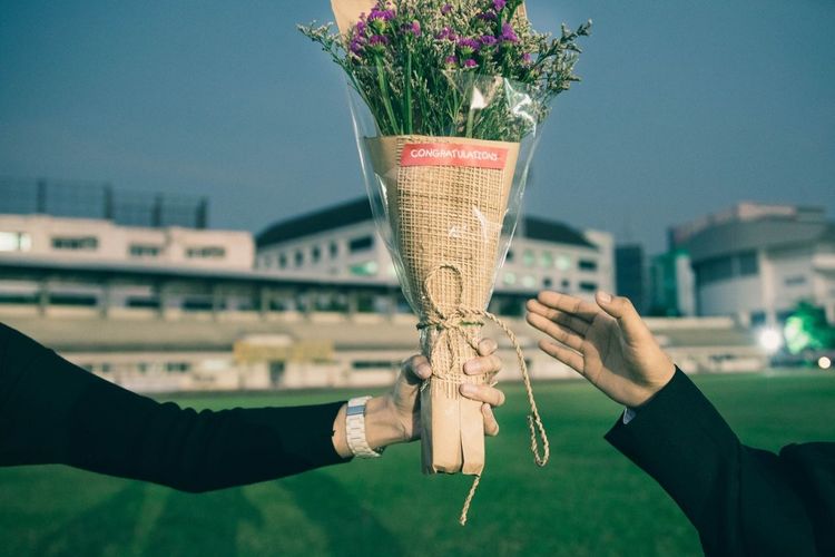 Cropped image of man giving bouquet to woman at stadium