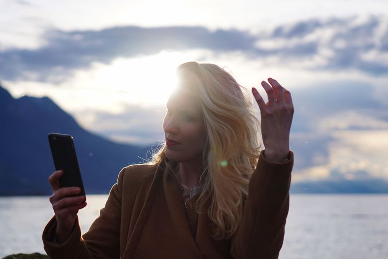 Mid adult woman using smart phone against lake