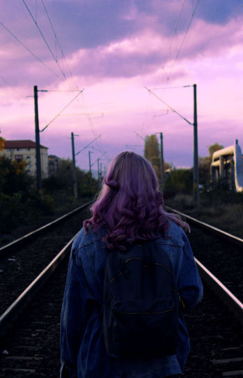 Rear view of woman standing on railroad track against sky during sunset