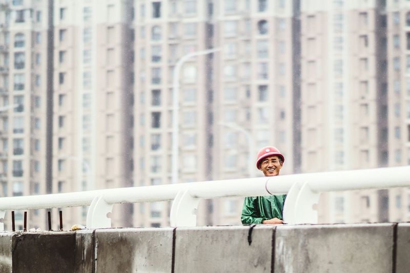 Portrait of happy man standing on bridge against buildings