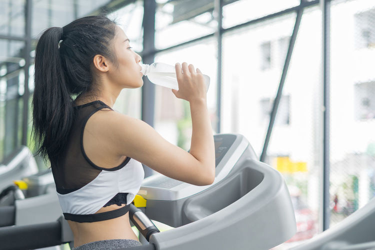 Young woman drinking water from bottle at gym