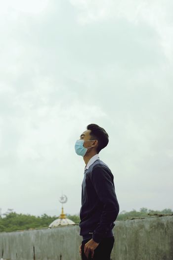 Side view of young man looking away against sky
