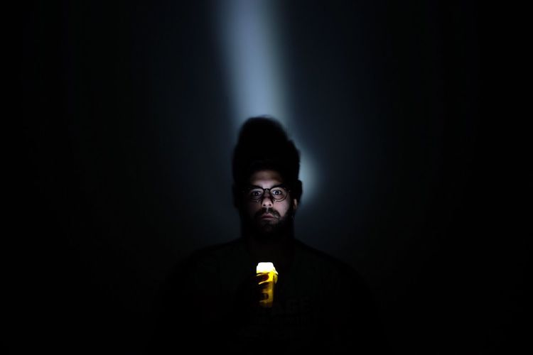 Portrait of young man holding illuminated flashlight in darkroom