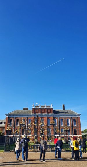 People walking on building against clear blue sky