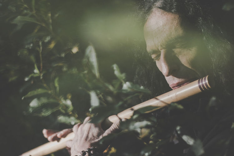 Man playing flute while standing in forest