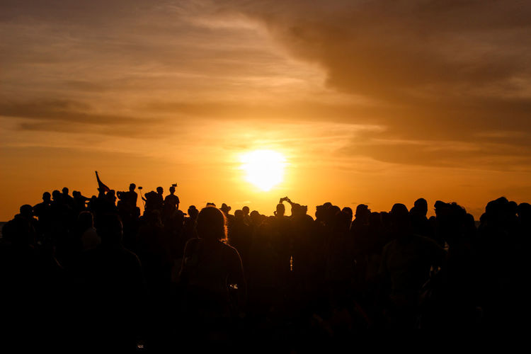 Silhouette crowd against cloudy orange sky during sunset