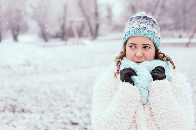 Young woman looking away while standing at park during winter