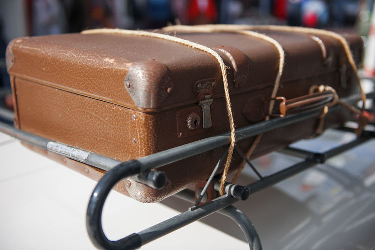 Close up of an old brown suitcase tied with ropes on a roof rack.