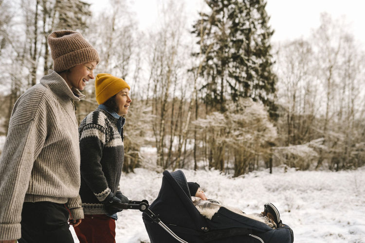 Mature woman pushing baby stroller while walking with girlfriend during winter