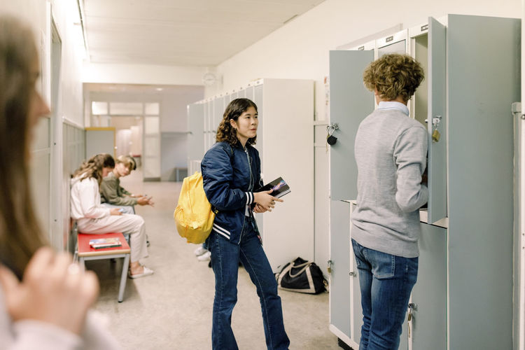 Teenage girl talking to boy standing near locker in school corridor