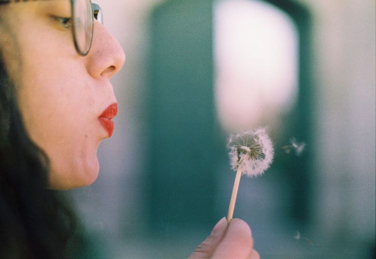 Close-up of woman blowing dandelion flower