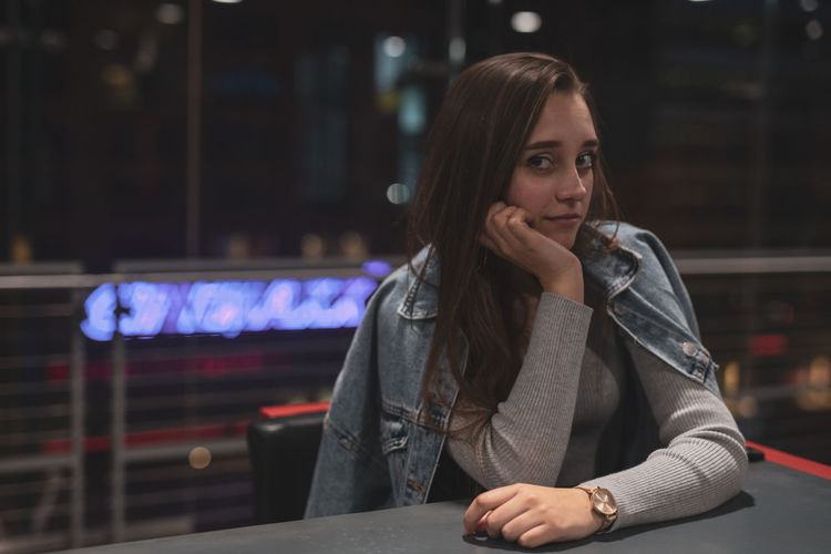 Portrait of beautiful young woman leaning on elbows over table at night