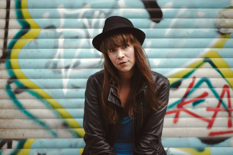 Portrait of woman wearing hat against graffiti shutter in city