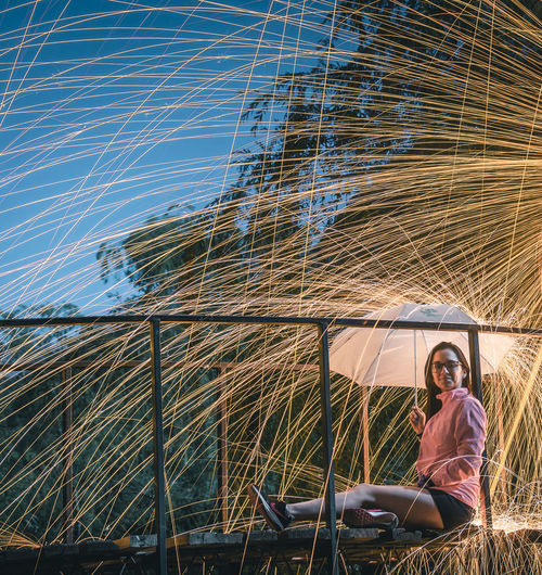 Woman sitting on bridge with umbrella under shower of sparks