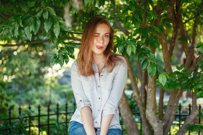 Portrait of young woman sticking out tongue while sitting by tree
