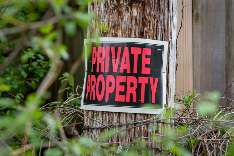 Private property sign on old post with barbed wire and thorn bushes