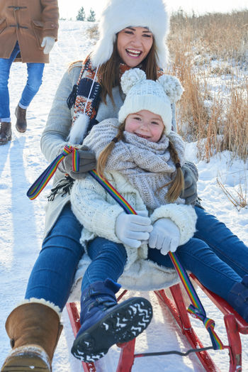 Man standing against mother and daughter sledding on snow covered field