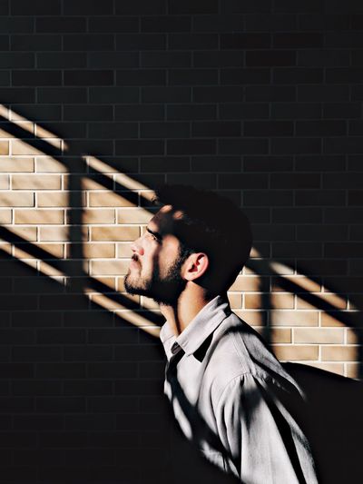 Side view of young man by wall