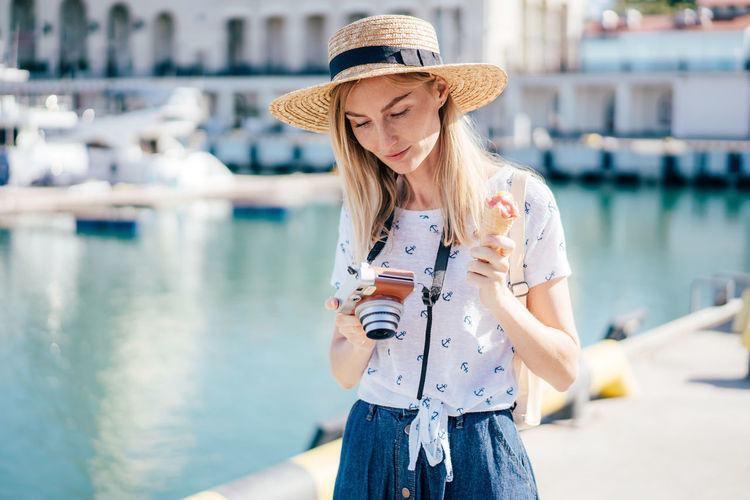 A young cute traveler in a european city with a camera and ice cream looks at an instant photo