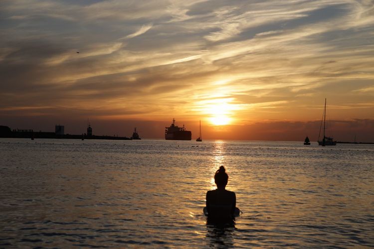 Rear view of woman in sea against sky during sunset