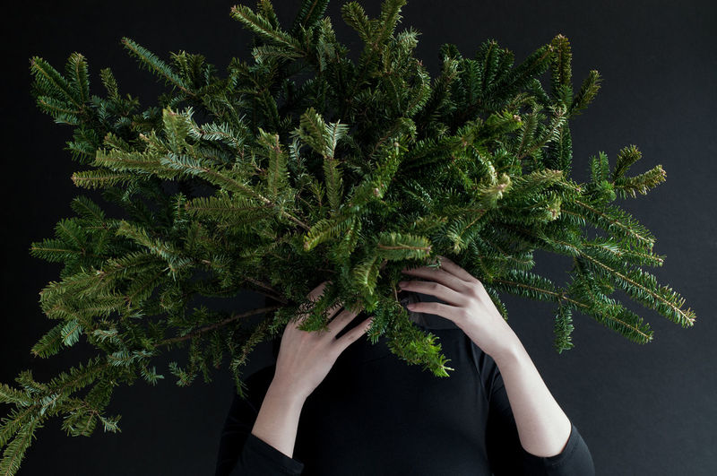 Woman holding pine tree branches against black background