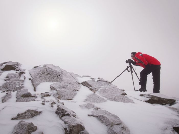 Man in warm clothes enjoy photographying in wild winter nature. snowy summit rock. listen to muse.