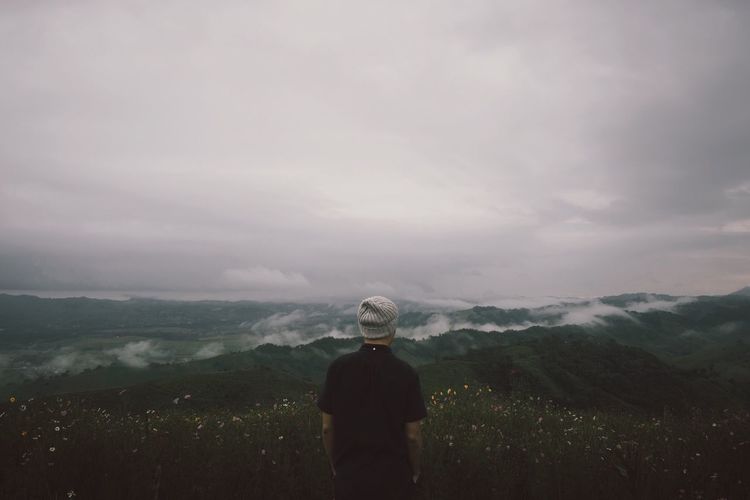 Rear view of young man standing on mountain against cloudy sky