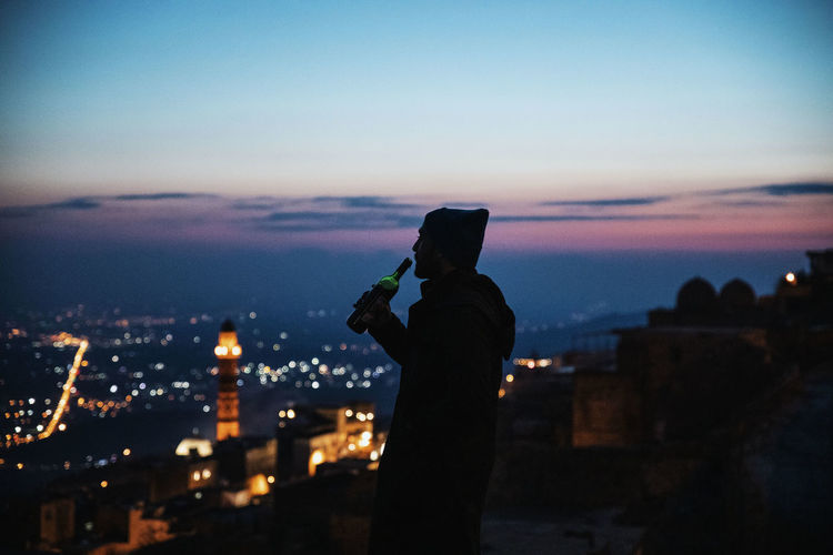 Silhouette man having wine against sky at dusk