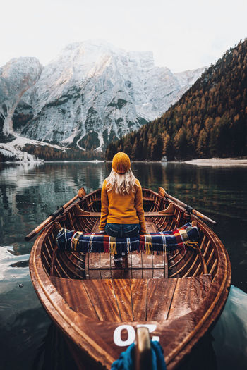Rear view of woman sitting on rowboat in lake against mountains